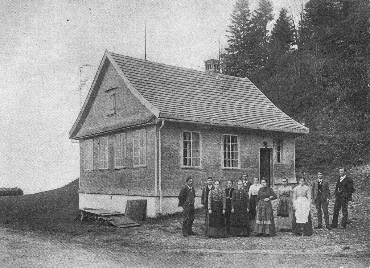 Eine Gruppe von Männern und Frauen steht vor einem alten Haus.